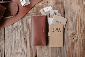 Flatlay of leather wallet and notebooks on a wooden surface, ideal for stationery enthusiasts.