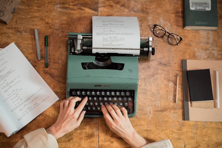 Hands typing on a classic typewriter with documents and stationery on a wooden table.