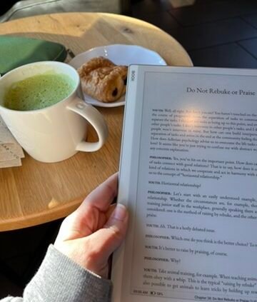Reading The Courage to Be Disliked on an e-ink device at a café table with coffee