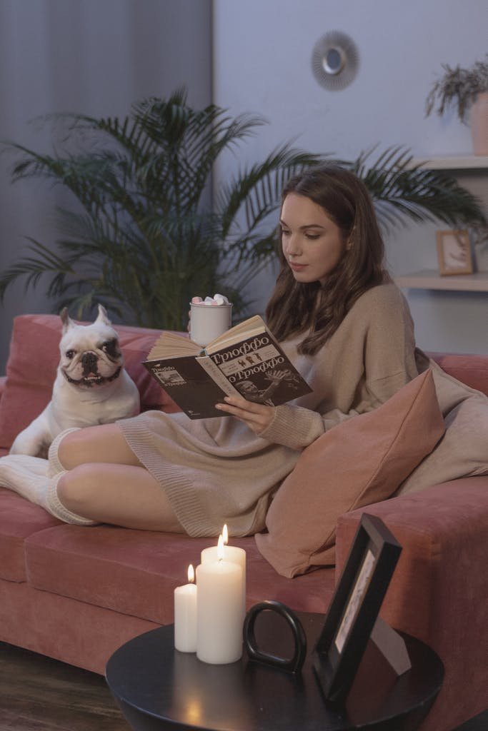 A woman enjoys a relaxing reading moment with her French Bulldog in a cozy living room setting.