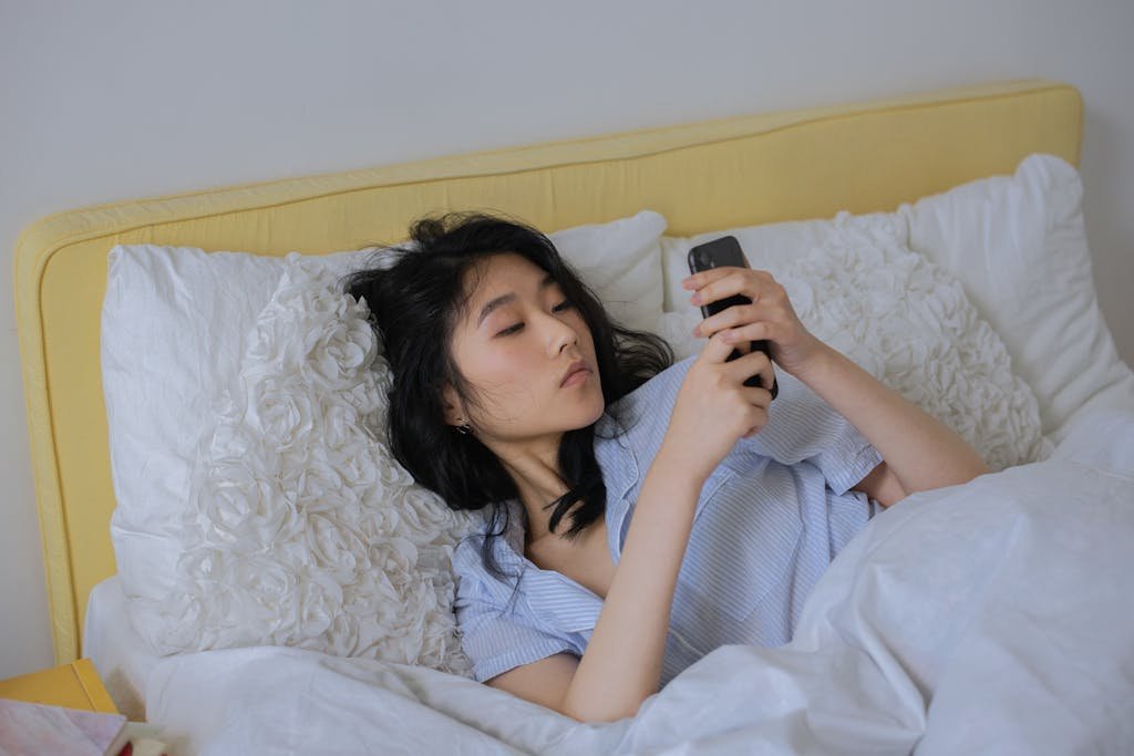 Asian woman comfortably lying in bed, not knowing how to stop scrolling her phone.