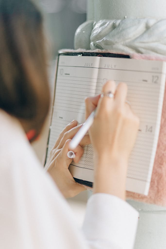 Close-up of woman writing in a planner with pen on July page.