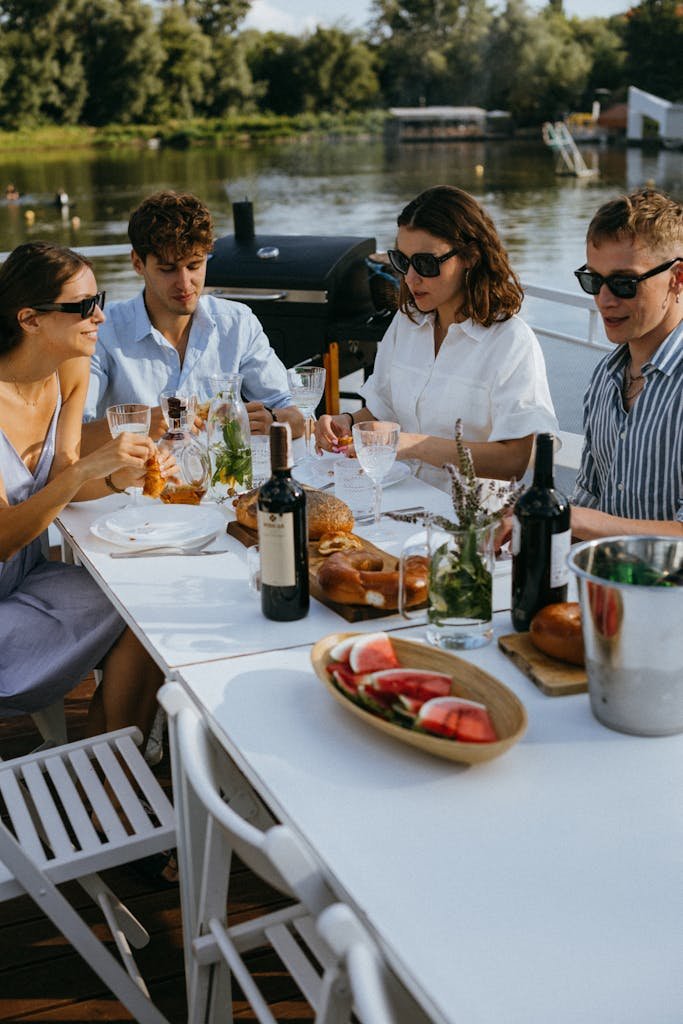 Four young adults enjoying a meal with wine on a yacht by the river.