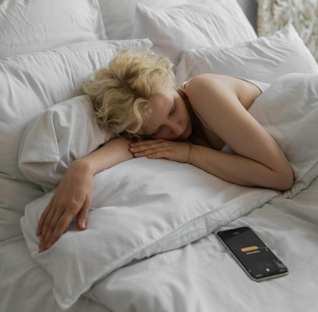 Lazy female resting in bed under soft blanket with alarm on cellphone for waking up