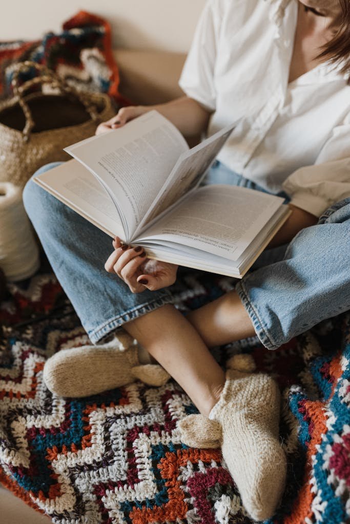 Person sitting comfortably while reading, surrounded by cozy knit and crochet items.