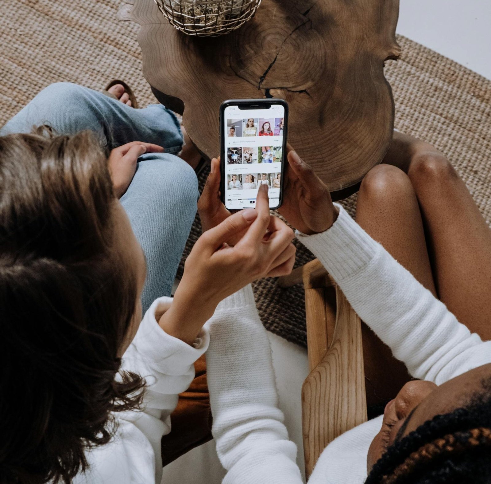 Two people looking at social media on a smartphone at a wooden table.