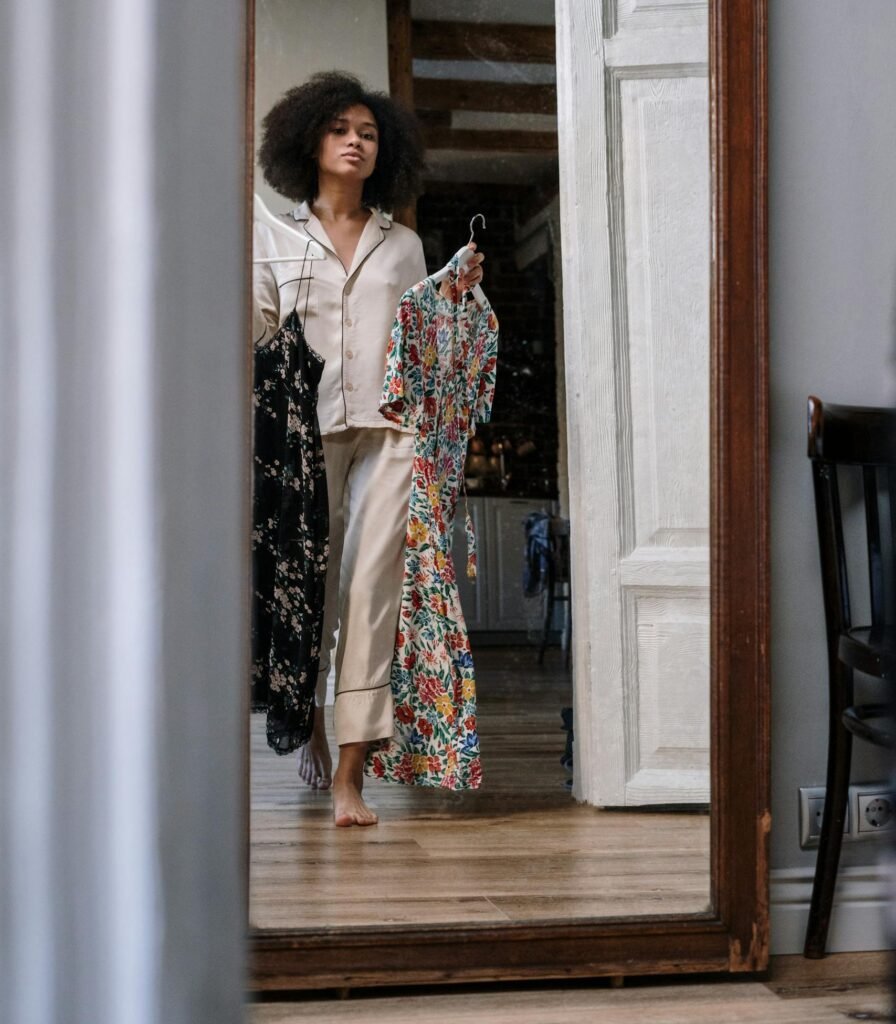 Woman choosing outfits reflected in a home mirror during morning routine.