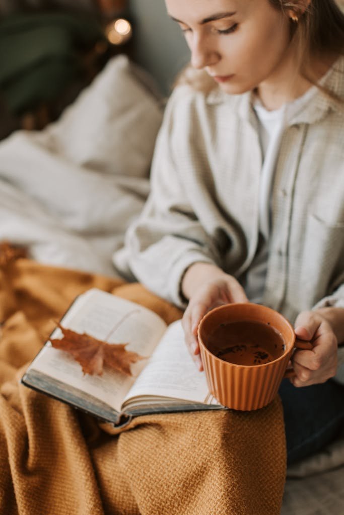 Woman enjoying a cozy autumn afternoon with a book, tea, and warm blanket.