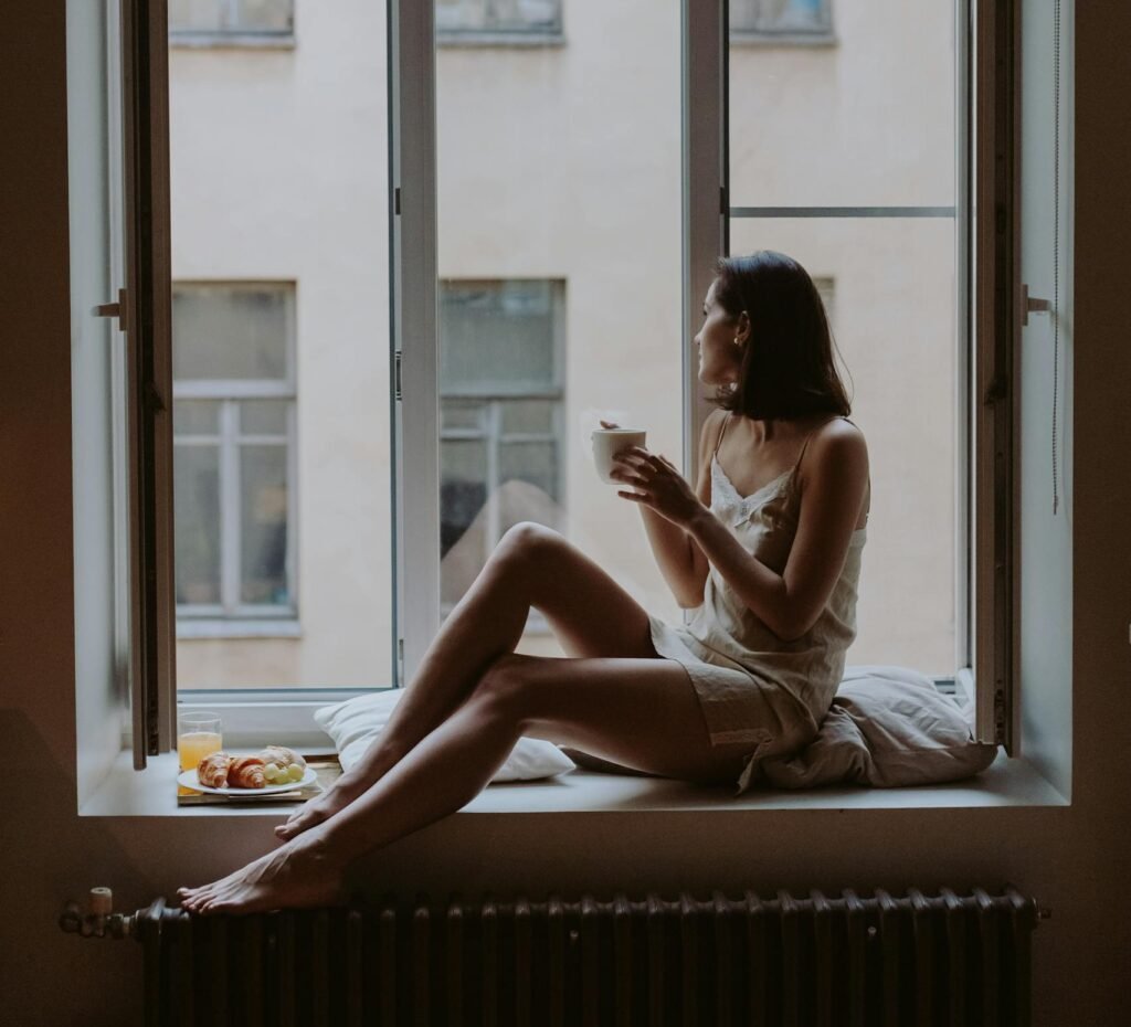 Woman enjoying a tranquil morning routine for success with coffee on a windowsill overlooking the city.