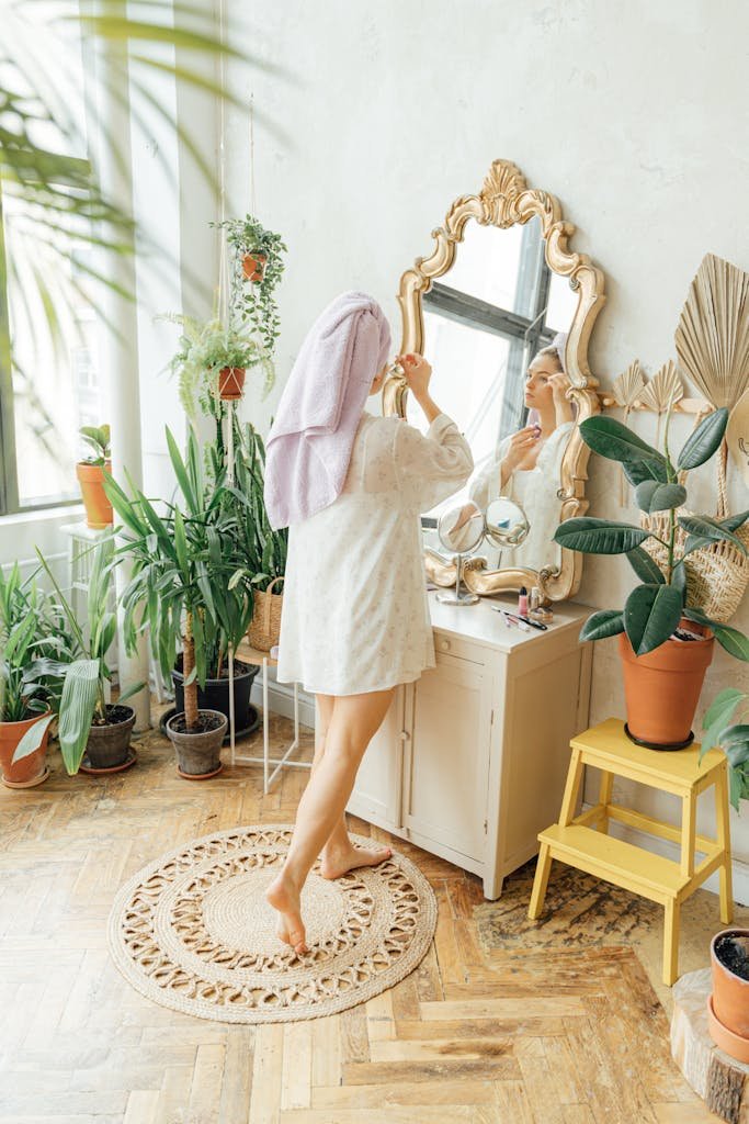 Woman in robe applying makeup in front of mirror surrounded by lush indoor plants.