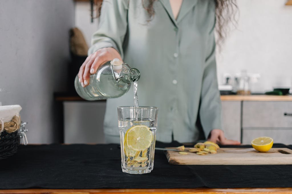 Woman pours water for lemon ginger infusion, promoting health and hydration for her morning routine for success.