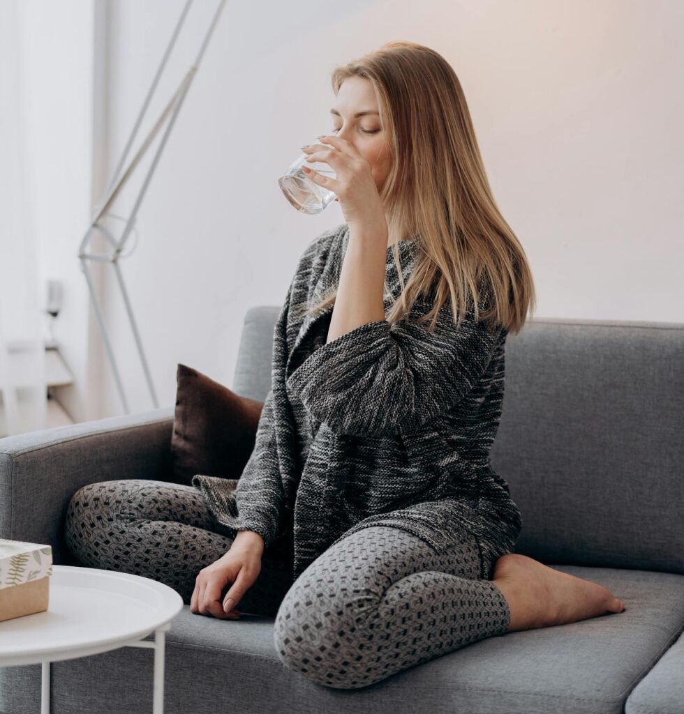 Woman relaxing on a sofa while drinking water in a stylish, cozy interior.
