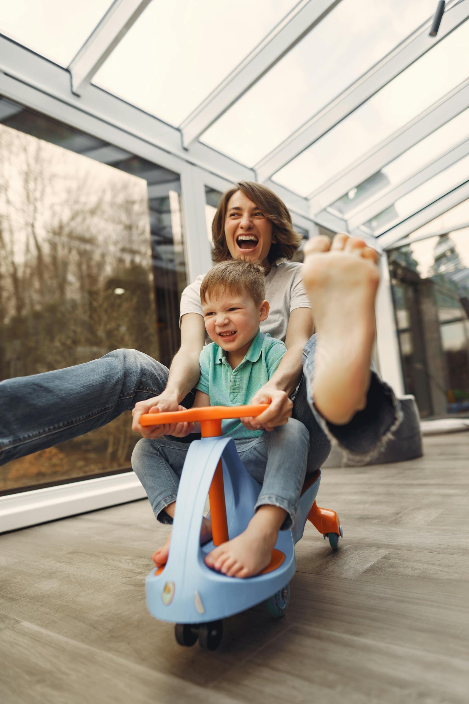 A joyful moment of a mother and son playing indoors on a toy car, showcasing a happy screen-free activity.
