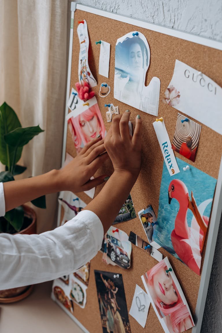 A person arranges inspirational cut-outs on a cork board for a vision board project.