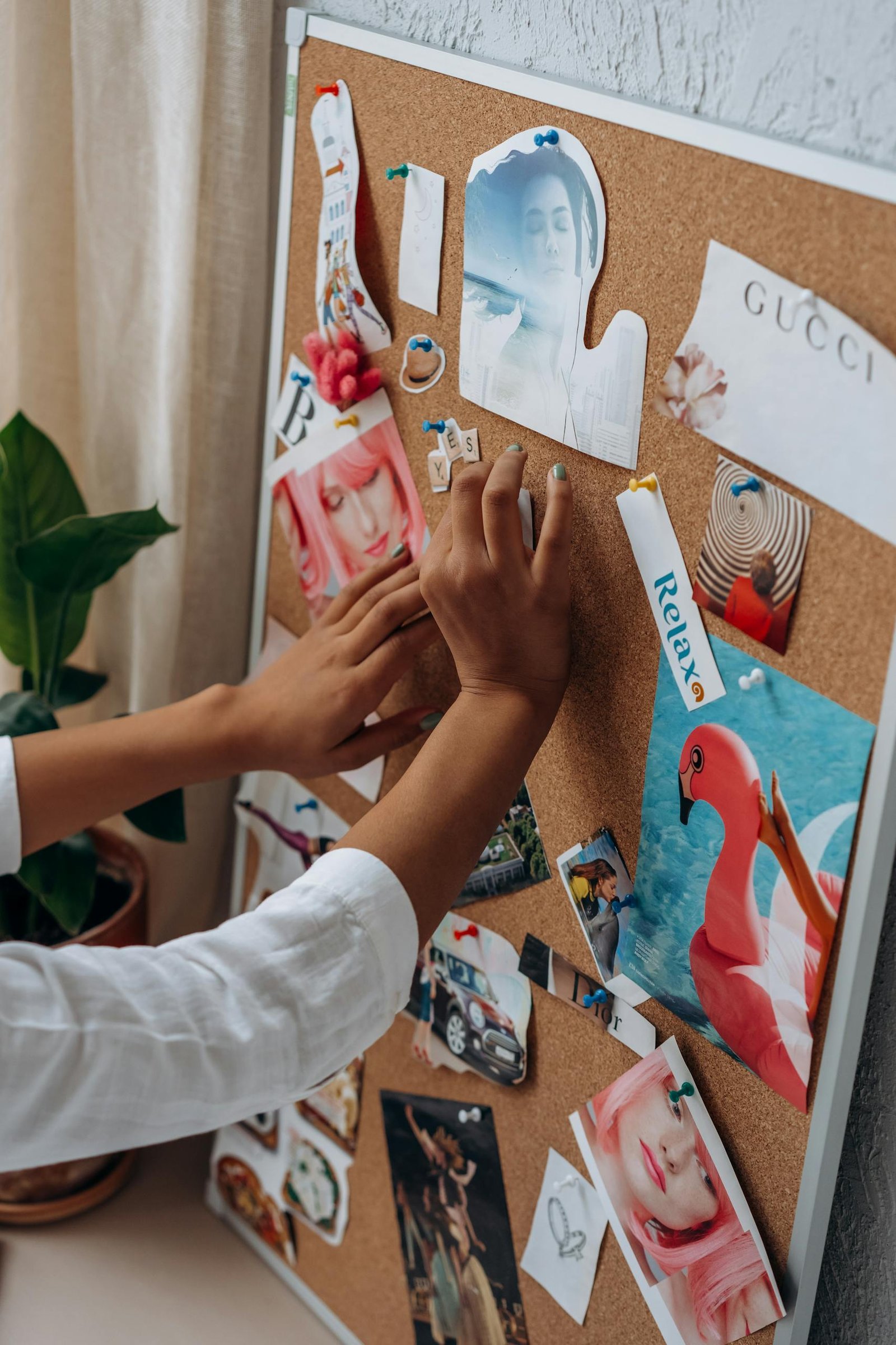 A person arranges inspirational cut-outs on a cork board for a vision board project.