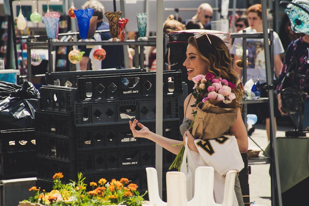 A woman joyfully shops at an outdoor market, holding roses.