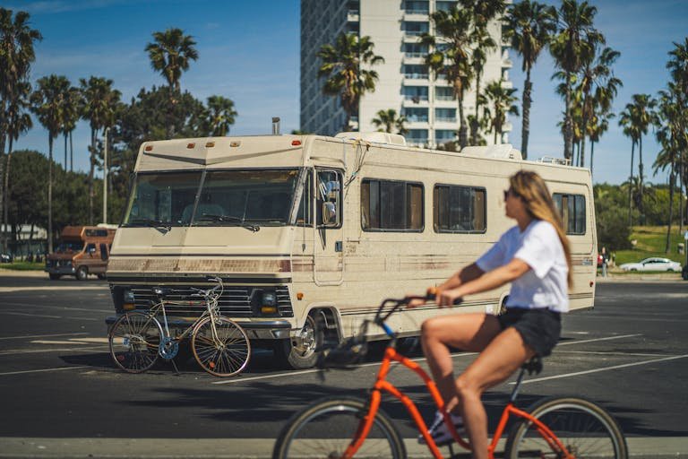 A woman rides a bike past a vintage motorhome parked along a palm-lined street in Santa Monica, CA.