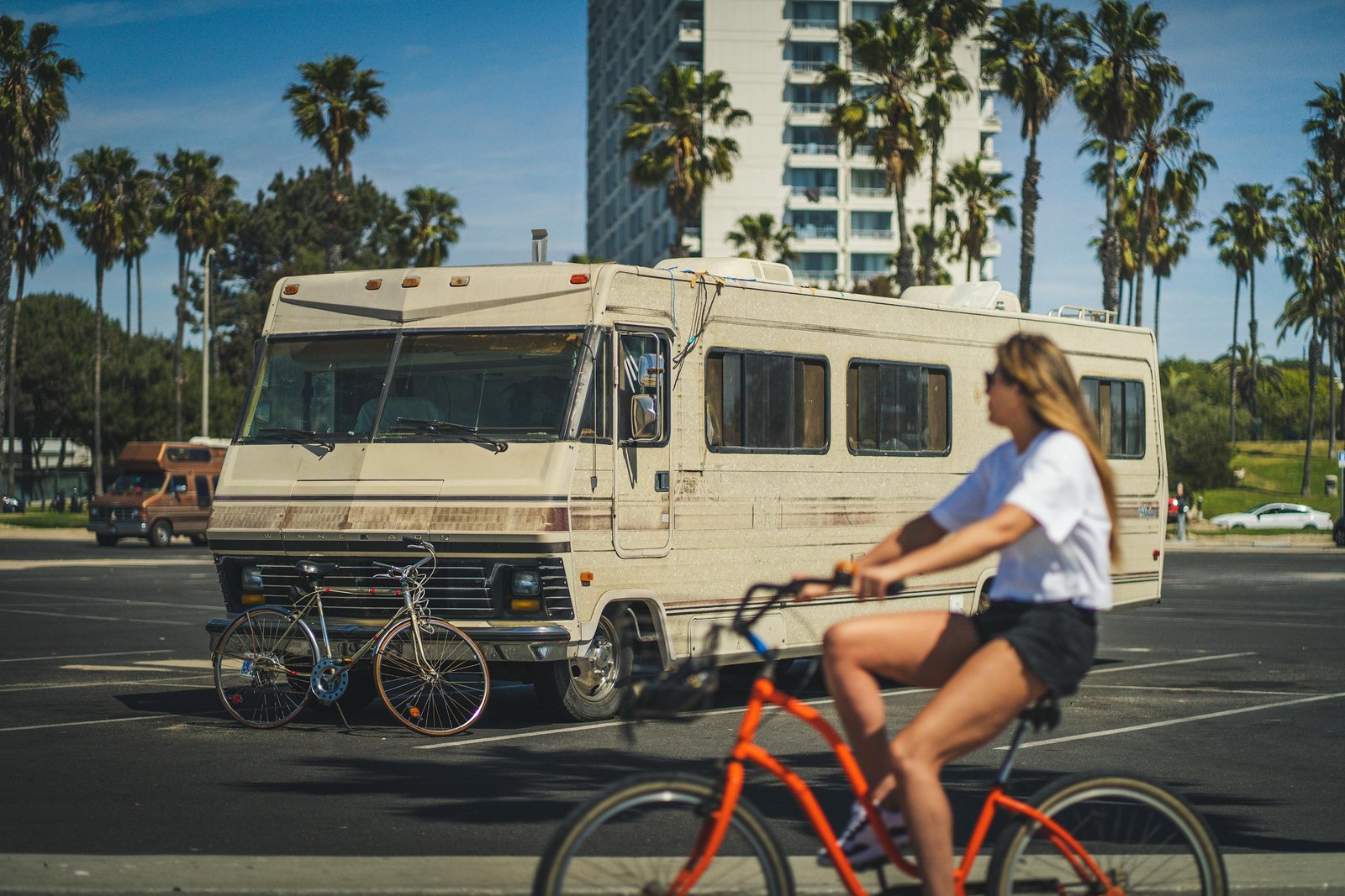 A woman rides a bike past a vintage motorhome parked along a palm-lined street in Santa Monica, CA.