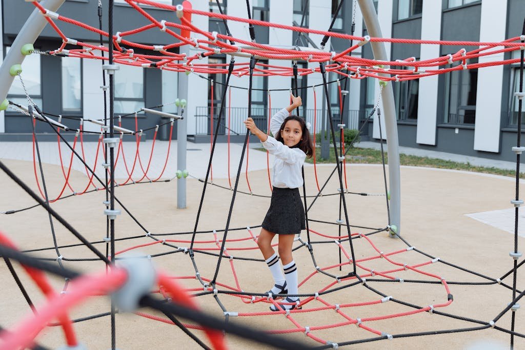 A young girl enjoys climbing on a vibrant jungle gym in an urban playground setting.