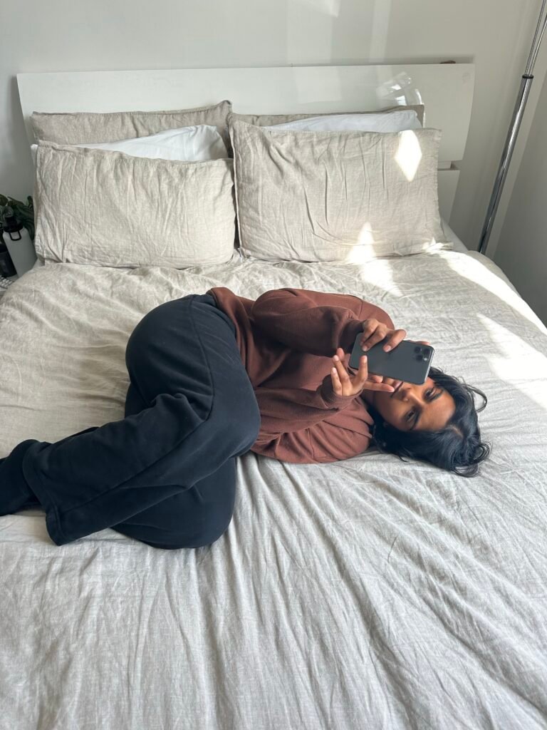 Woman in a beige bedroom, scrolling in her phone.