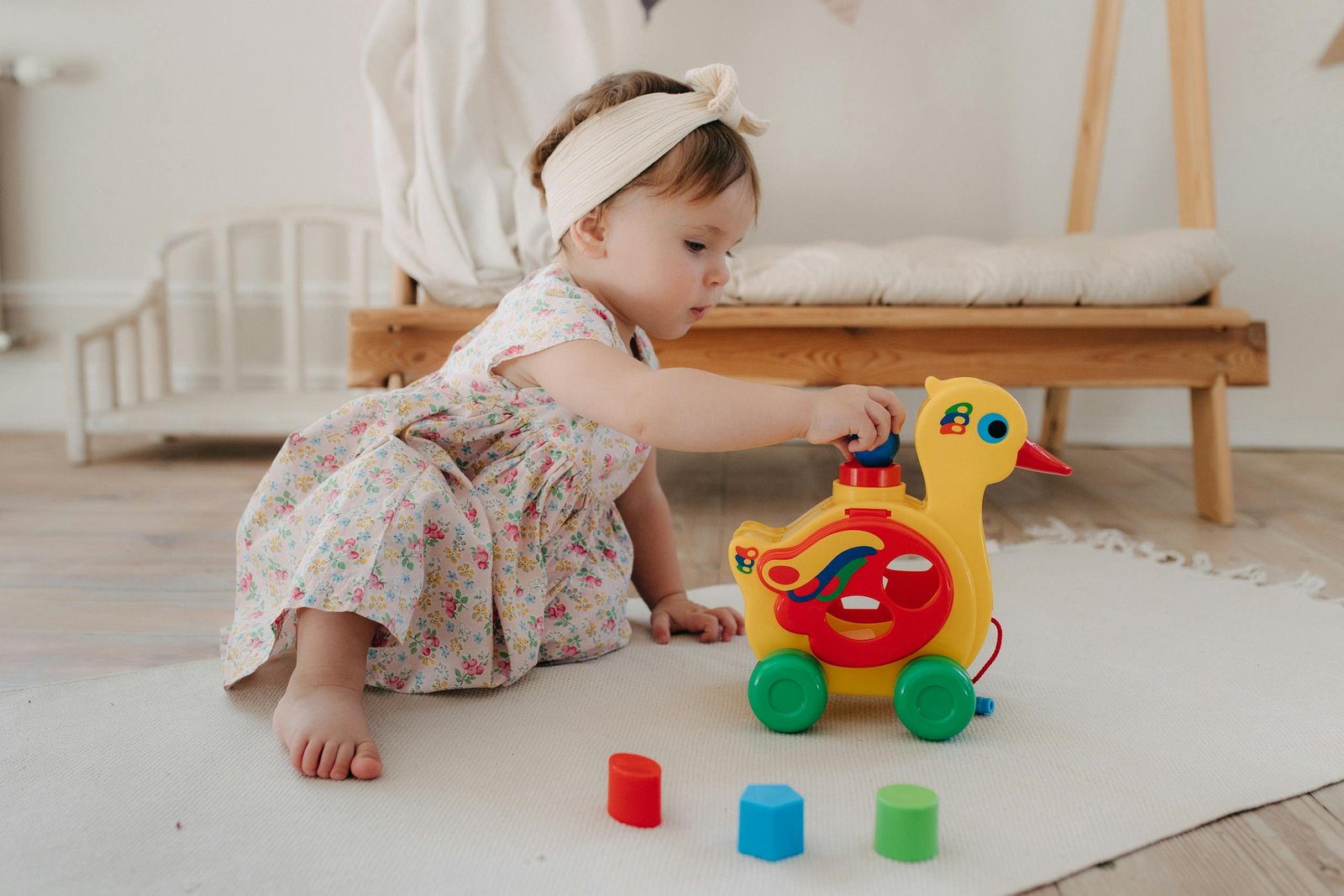 Cute baby girl in a floral dress playing with a colorful duck toy indoors.