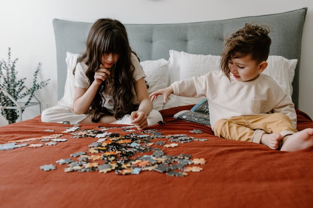 Two children playing with jigsaw puzzles on a cozy bed indoors.