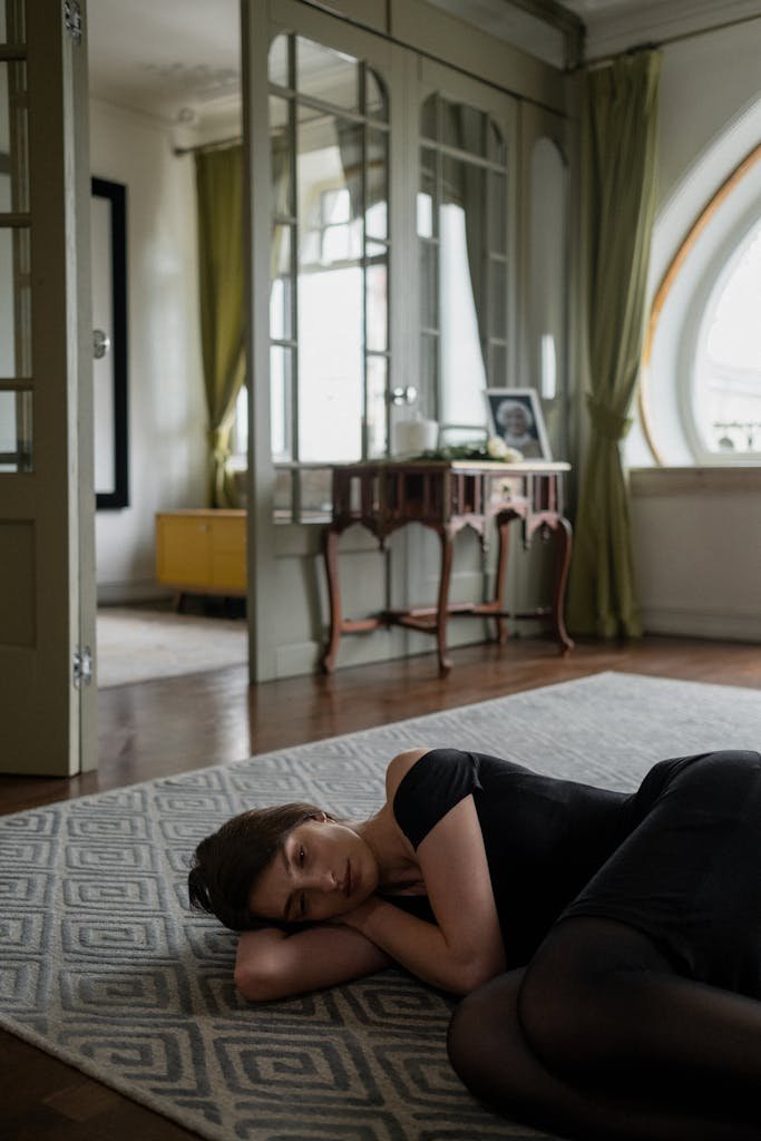 Woman in a black dress lying on a rug in an elegantly decorated room, conveying a sense of peace.