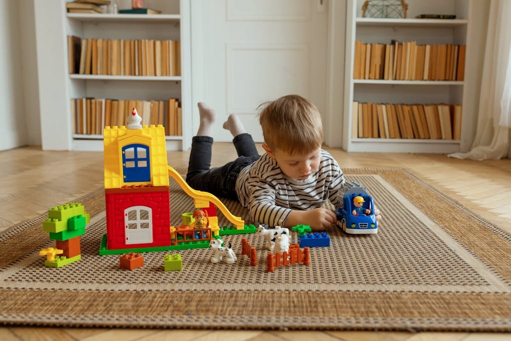 Young child playing with colorful building blocks and toy car on a woven carpet in a home setting.