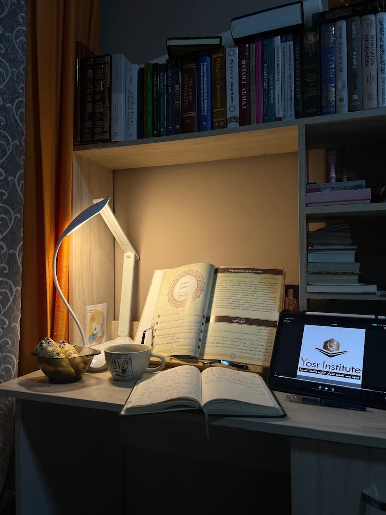 A cozy home office setup with open books, a tablet, and a warm lamp lighting.