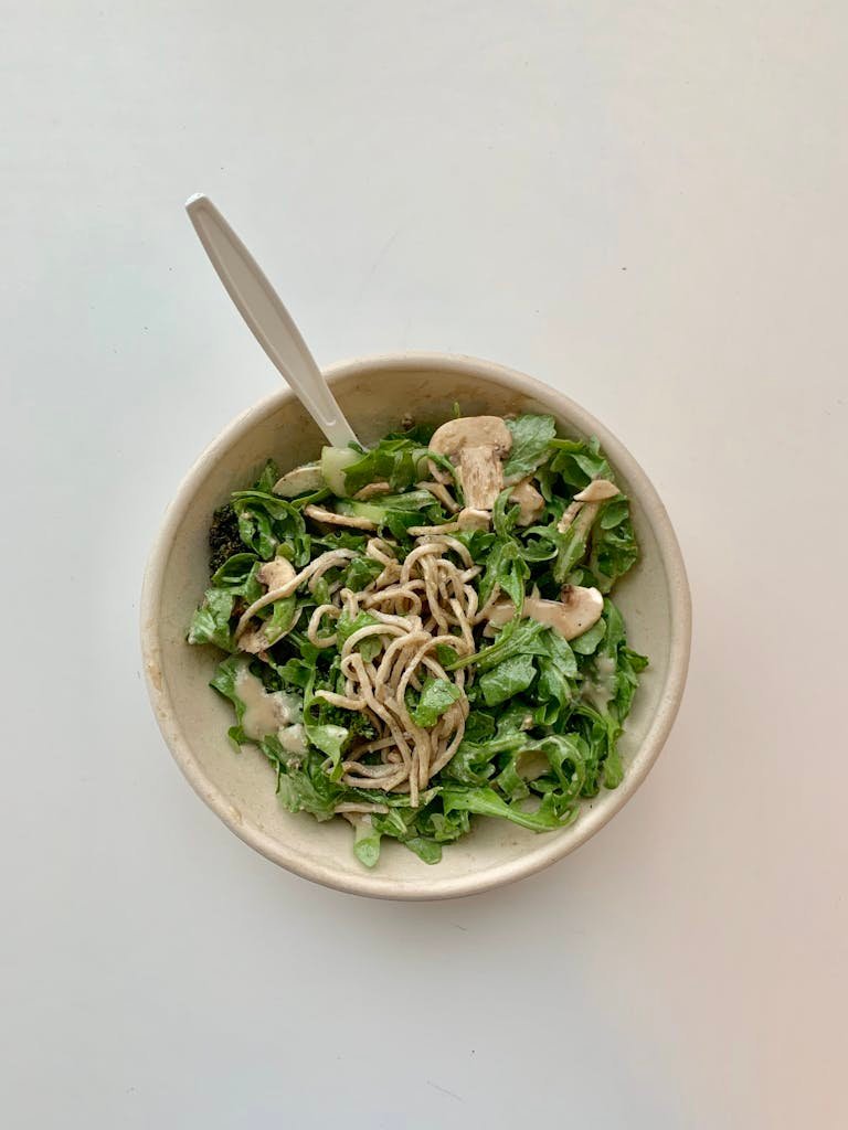 Delicious noodle salad with mushrooms, arugula, and greens in a textured bowl.