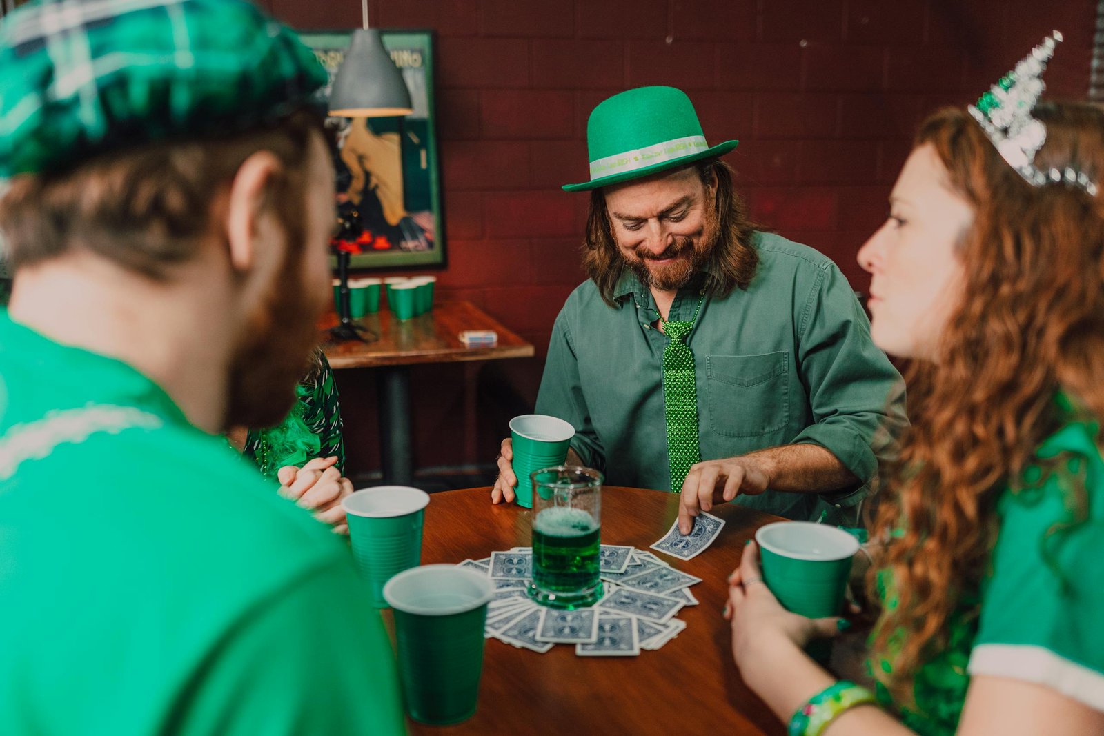 Group of friends enjoying St. Patrick's Day with drinks and card games indoors.