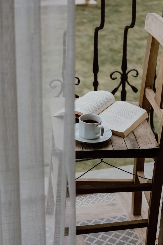 Relaxing morning scene with coffee and book on a wooden chair on a peaceful balcony.