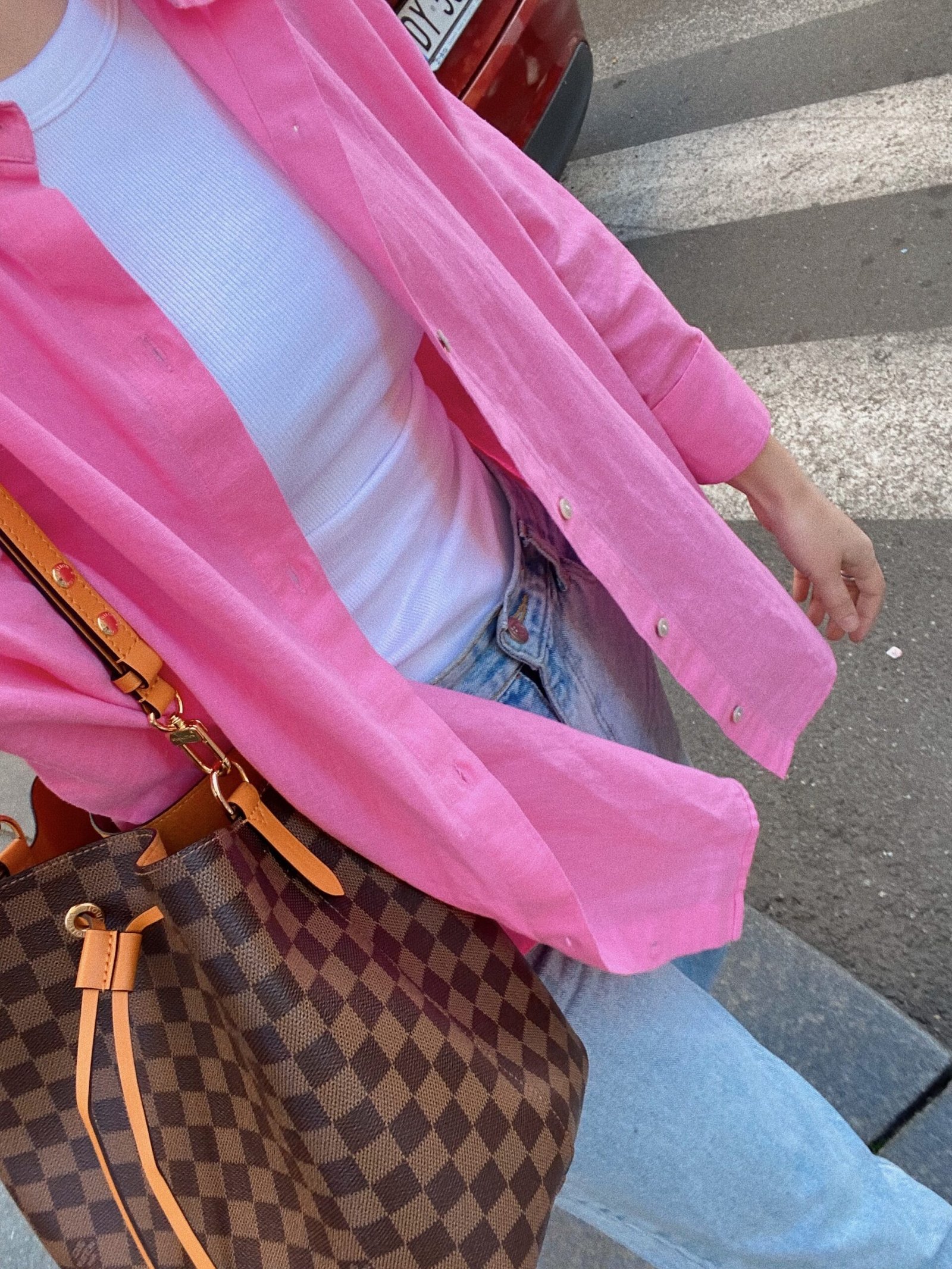 Casual spring outfit with pink shirt, white tank top, jeans, and brown checkered bag.