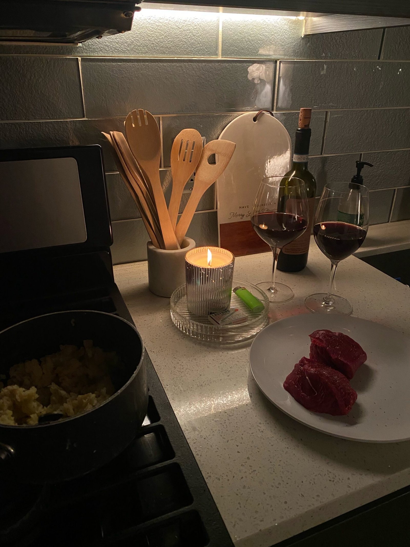 Cozy candlelit kitchen scene with red wine, steak, and wooden utensils during a romantic weeknight dinner at home.