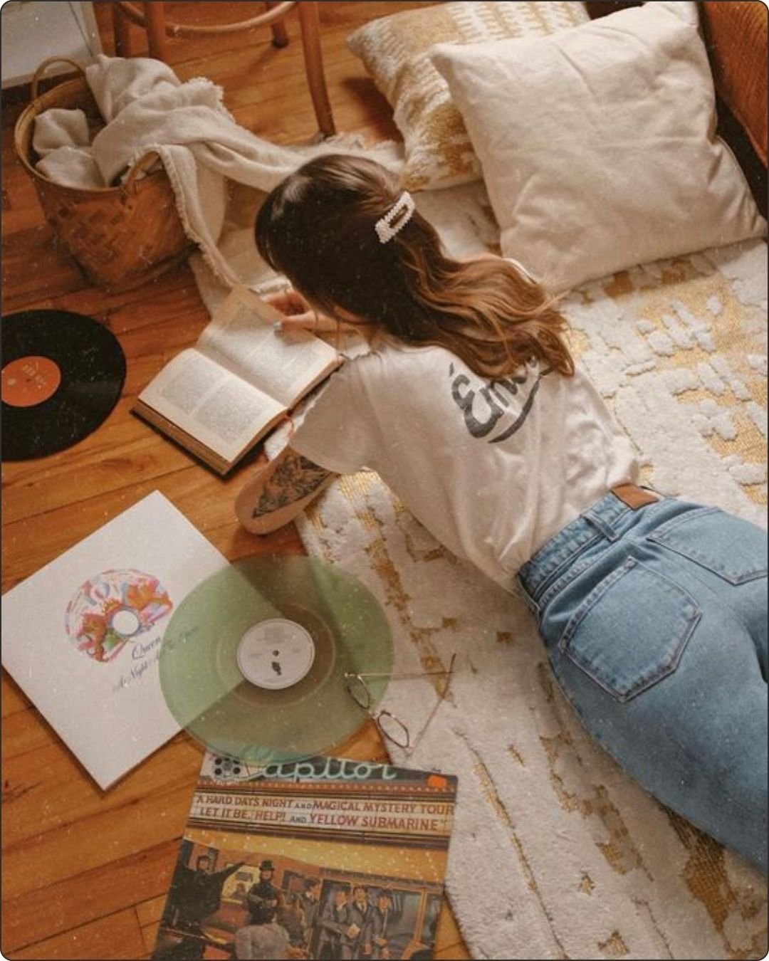 Woman laying on the flor next to a vinyl and reading a book, enjoying her analog hour