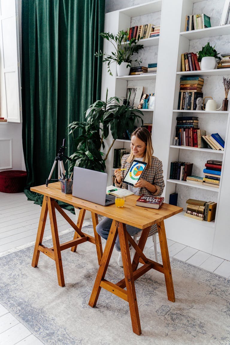 A woman at her home office desk using a laptop and tablet, creating a productive workspace.