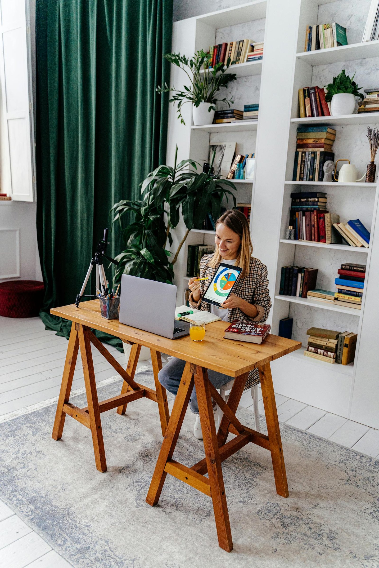 A woman at her home office desk using a laptop and tablet, creating a productive workspace.