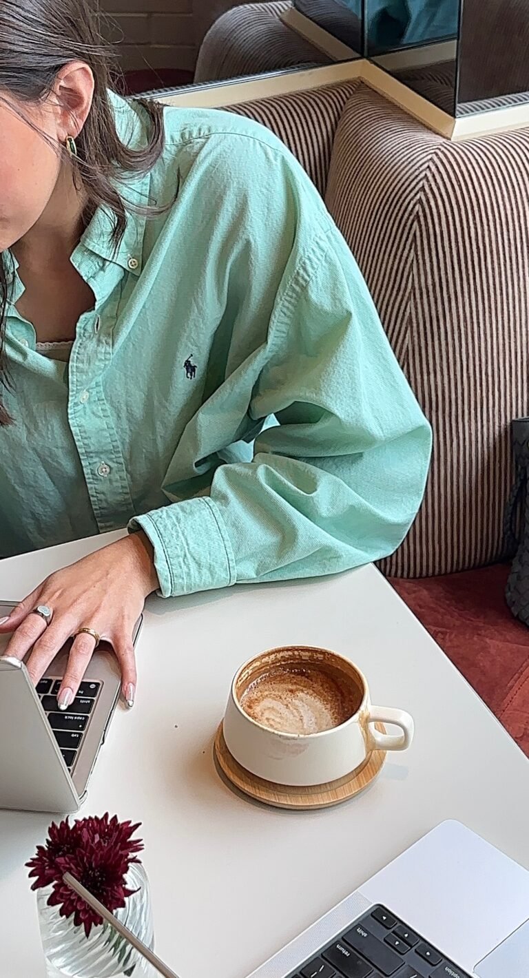 Woman working on laptop with coffee at a cozy café, representing gentle ambition and a sustainable career pace